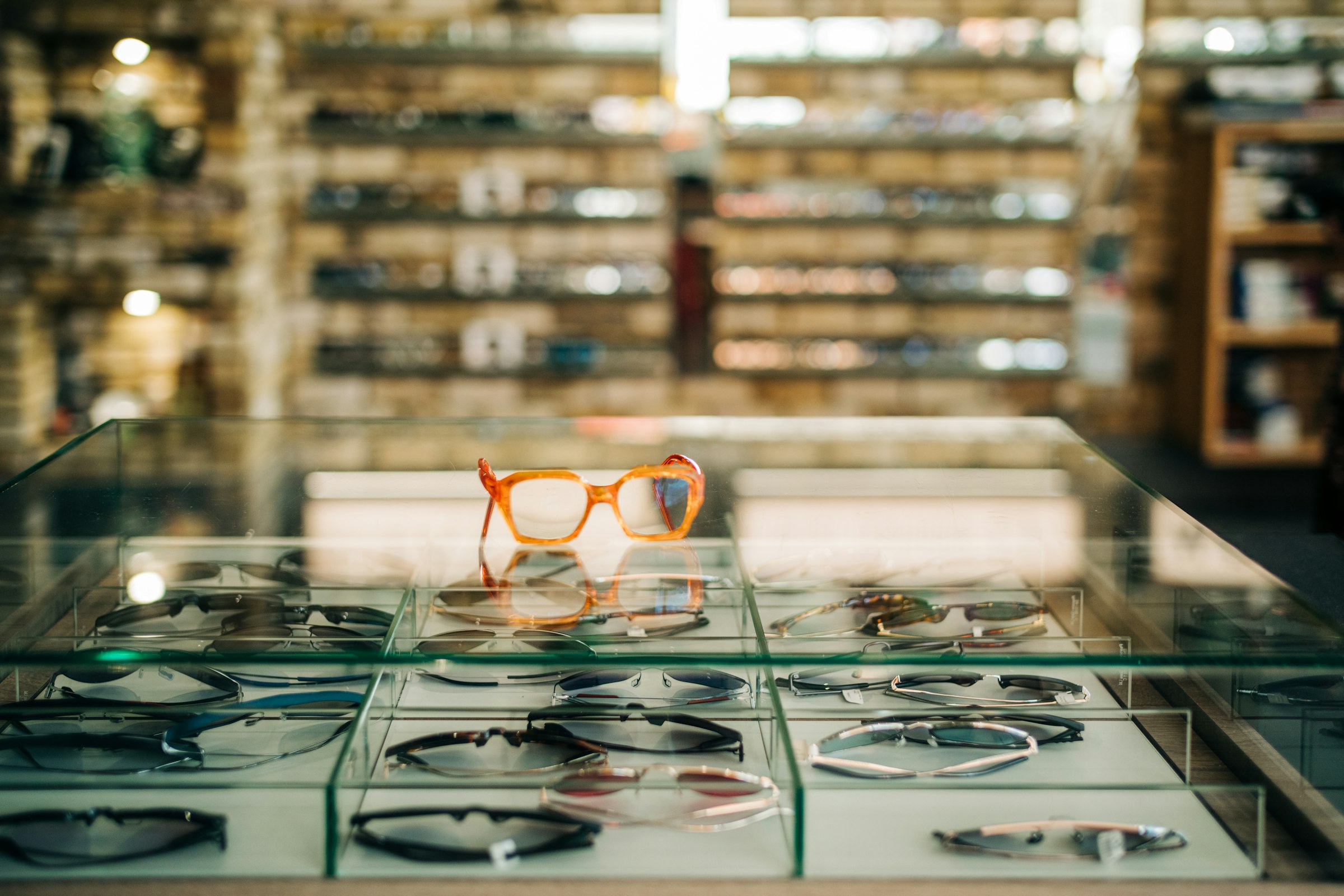 A glass display case of frames in an optical centre, the frame wall lit behind it