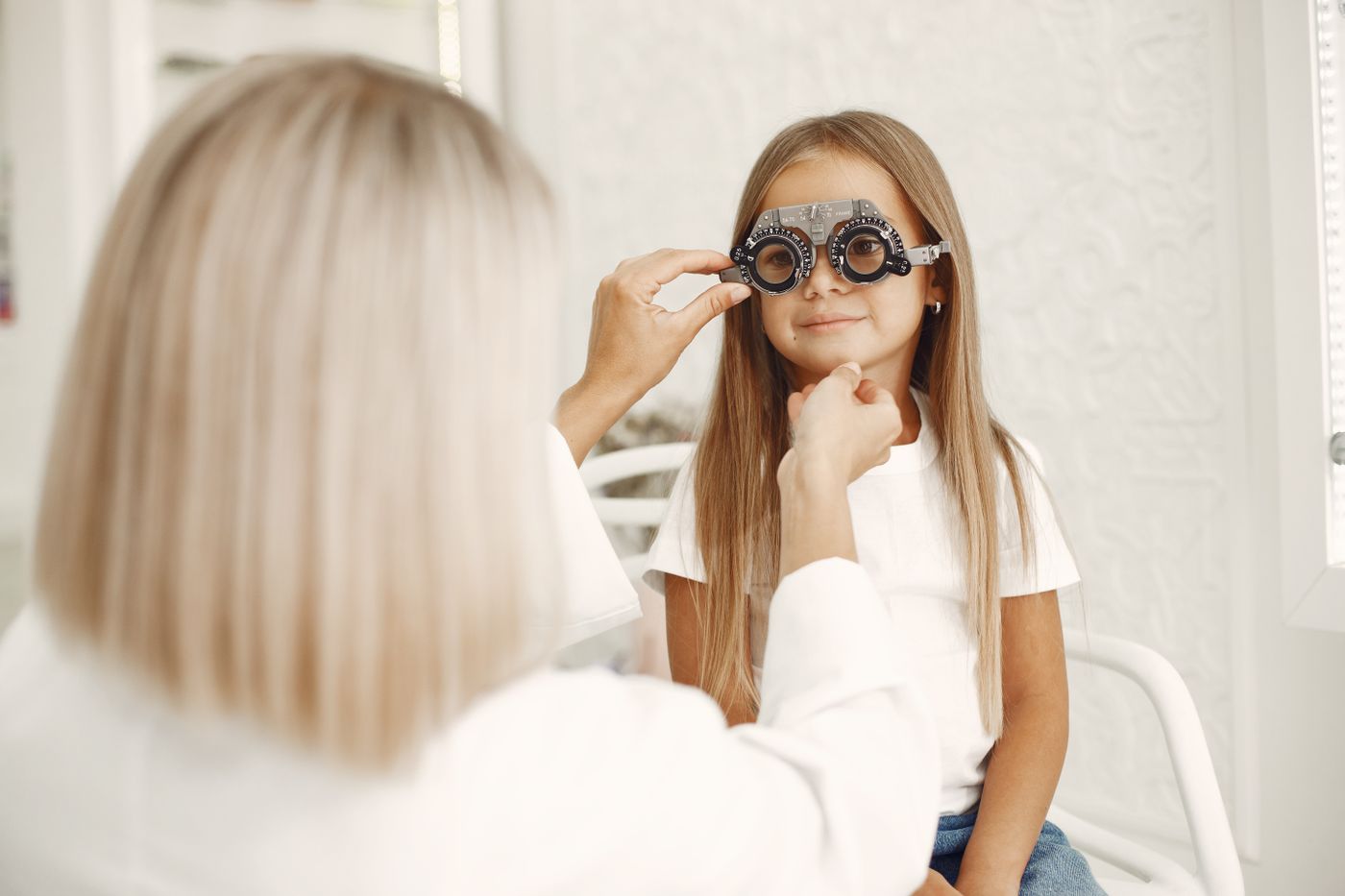 An optometrist holding a trial frame in front of a young girl's eyes during a check-up