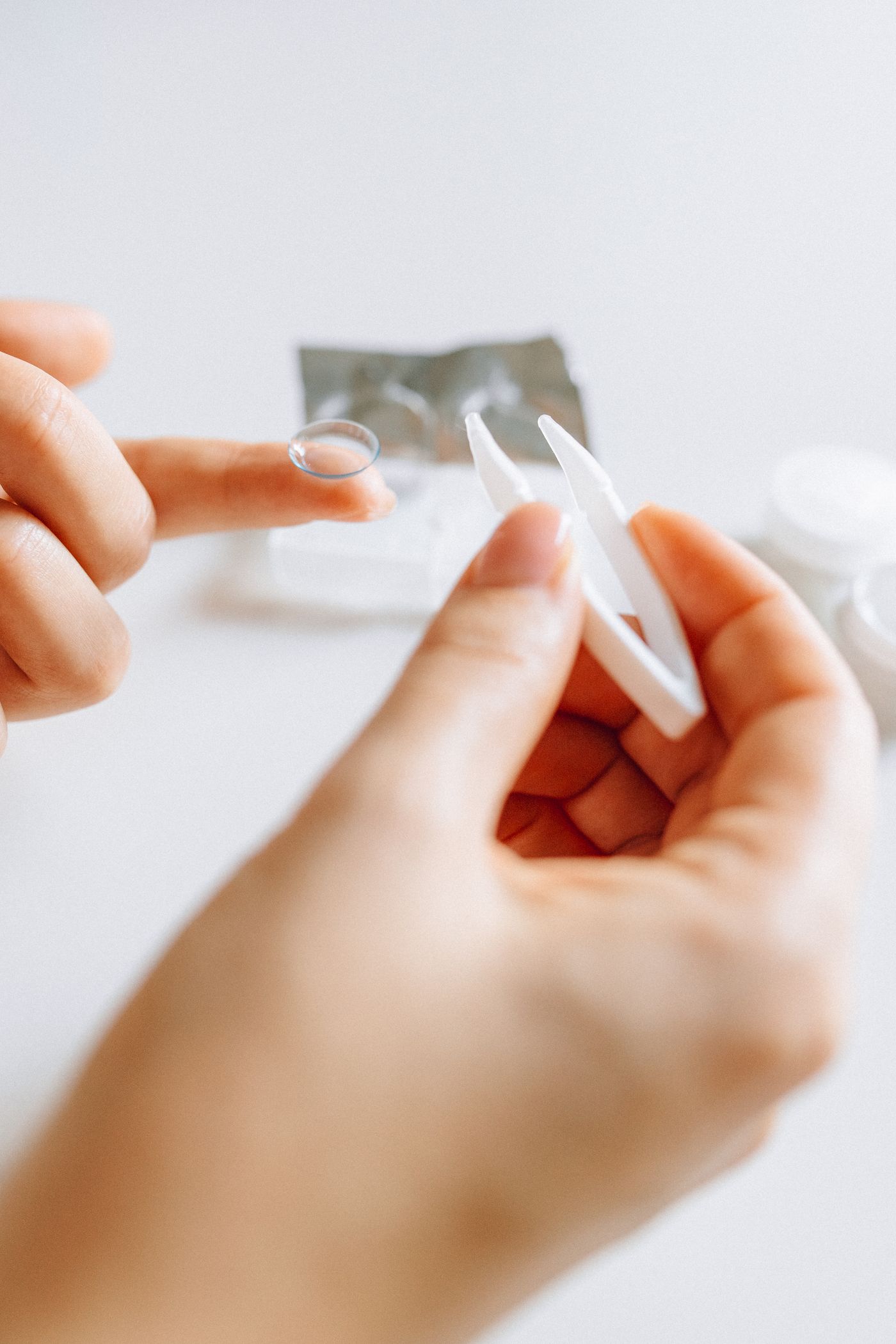 A daily disposable contact lens balanced on a fingertip beside its blister pack