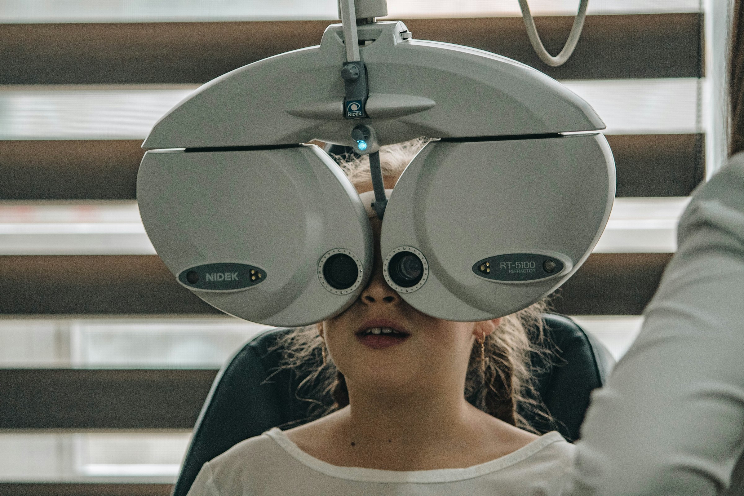 A girl seated behind a digital automated refractor while the optometrist steps her through the lenses